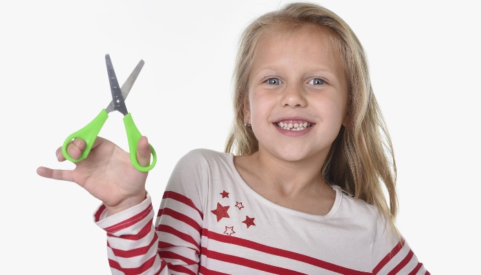A young girl in a striped shirt holding a pair of safety scissors.