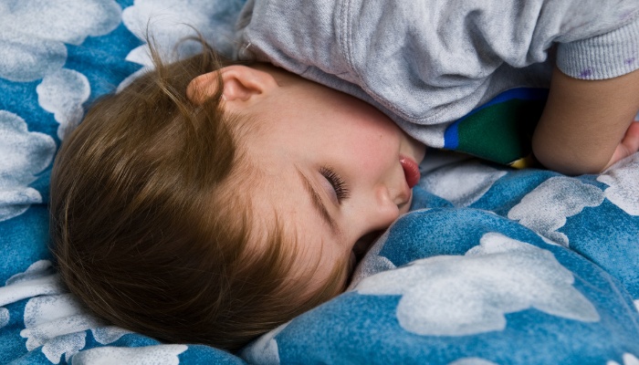 A toddler sleeping on bedding decorated with clouds.