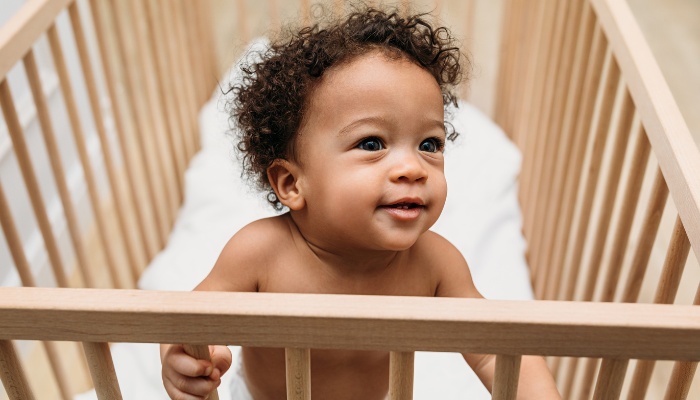 A wide-awake toddler standing up in his crib wearing only a diaper.