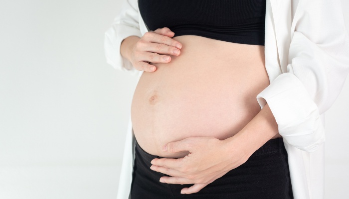 A woman with her hands on her pregnant belly against a white background.
