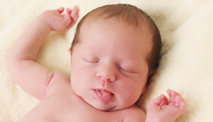 A newborn baby sleeping with arms up and tongue hanging out.