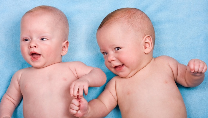 Fraternal twin brothers wearing only diapers against a blue background.