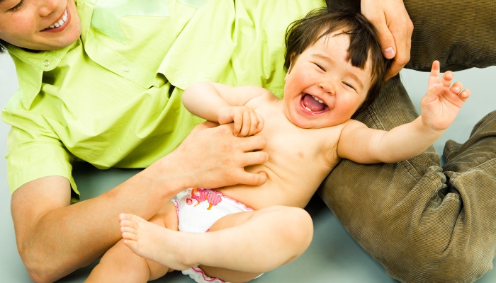 A parent on the floor tickling his happy baby.