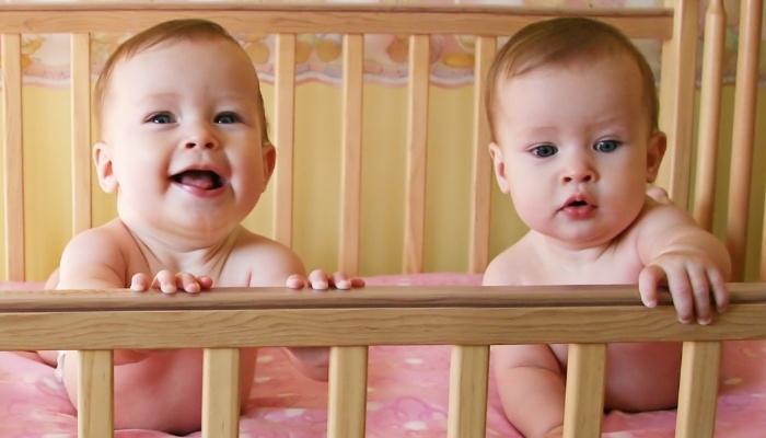 Twin babies lying on their tummies in their crib.