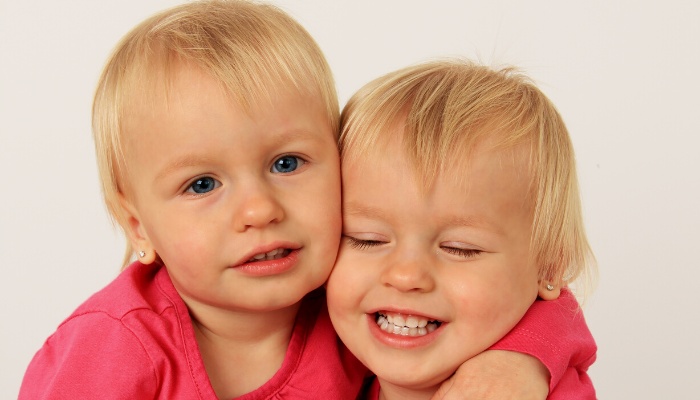 Two twin sisters in pink hugging each other.