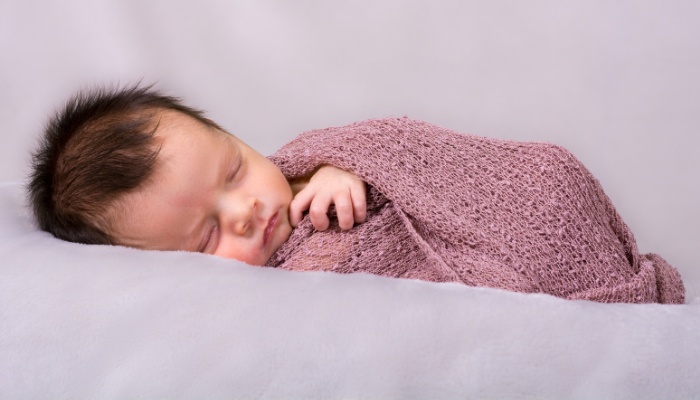 A newborn baby girl wrapped in a soft mauve blanket.
